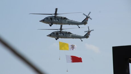 Zwei Hubschrauber fliegen mit den Flaggen vom Vatikan sowie Bahrain / © Cindy Riechau (dpa)