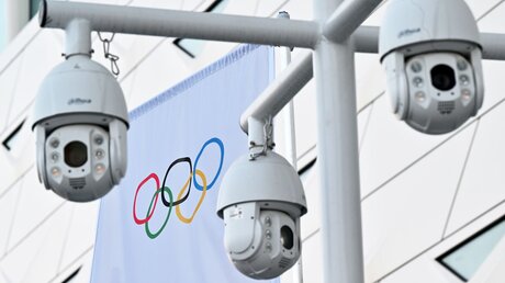 Peking: Die olympischen Ringe auf einer Fahne sind hinter den Sicherheitskameras zu sehen / © Peter Kneffel (dpa)