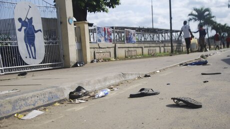 Flip Fops und Sandalen liegen nach einer Massenpanik auf einer Straße. Bei einer Massenpanik kurz vor Beginn einer Kirchenveranstaltung in Nigeria sind nach Polizeiangaben mehrere Menschen ums Leben gekommen / © Uncredited/AP (dpa)