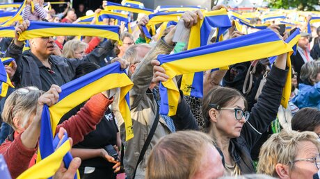 Teilnehmer halten gelb-blaue Schals in den Nationalfarben der Ukraine in die Höhe bei einem Gebet auf der Eröffnung des 102. Deutschen Katholikentags, am 25. Mai 2022 in Stuttgart. / © Harald Oppitz (KNA)