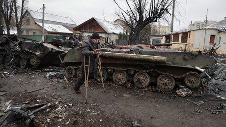  Ukraine, Butscha: Ein Mann auf Krücken geht an den Überresten eines russischen Militärfahrzeugs vorbei / © Serhii Nuzhnenko (dpa)