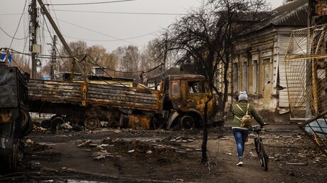 Ukraine, Trostyanets: Eine Frau fährt mit ihrem Fahrrad um zerstörte russische Fahrzeuge in Trostyanets / © Daniel Carde (dpa)