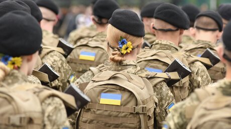 Ukrainische Soldaten, in deren Mitte zwei Soldatinnen mit in den ukrainischen Nationalfarben gehaltenen Blumenschmuck im Haar stehen / © Bumble Dee (shutterstock)