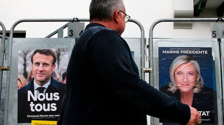 Vor Präsidentschaftswahl in Frankreich geht ein Mann an Wahlplakaten des amtierenden Präsidenten Macron und seiner Herausforderin Le Pen vorbei / © Bob Edme (dpa)