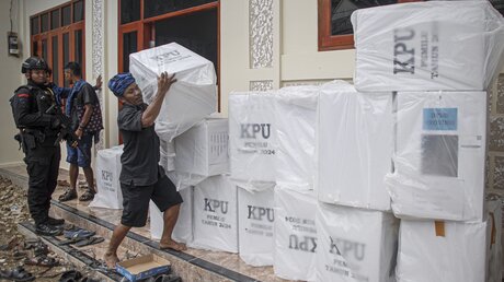 Vor der Wahl in Indonesien steht ein Polizist Wache, während ein Arbeiter die Wahlurnen ordnet (dpa)