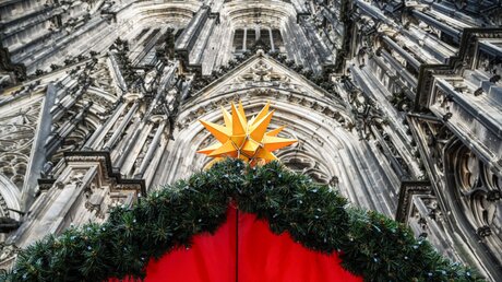 Weihnachtsstern an der Weihnachtsmarktbude, in der Gäste kleine Kerzchen anzünden können, vor dem Kölner Dom, der aus Sicherheitsgründen gesperrt ist, am 28. Dezember 2023 in Köln / © Harald Oppitz (KNA)