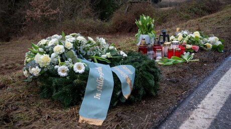 Kusel: Ein Kranz sowie Blumen und Kerzen liegen am Tatort an der Kreisstraße 22 bei Ulmet zum Gedenken / © Harald Tittel (dpa)