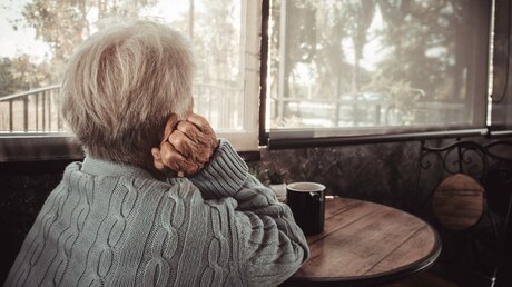 Eine Seniorin schaut aus dem Fenster / © AimPix (shutterstock)