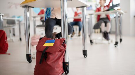 Ein Rucksack mit einem Aufkleber in den Farben der ukrainischen Flagge in einem Klassenraum / © Halfpoint (shutterstock)
