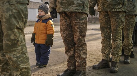 Ein Kind steht neben ukrainischen Soldaten und imitiert ihre Haltung / © Vadim Ghirda (dpa)