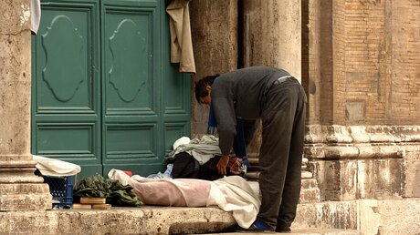 Ein Obdachloser hat sich vor einer verschlossenen Eingangstüre einer Kirche in Rom mit Decken ein Schlaflager gerichtet. / © KNA-Bild (KNA)