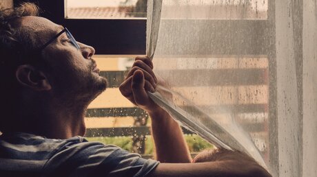 Mann blickt sehnsüchtig aus dem Fenster / © Kitja Kitja (shutterstock)
