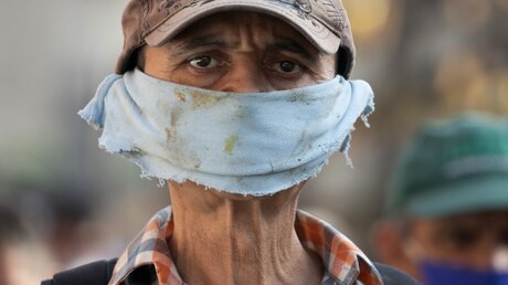 Ein Mann trägt ein Stück Stoff als Gesichtsmaske  / © Ariana Cubillos (dpa)