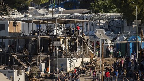 Migranten und Flüchtlinge stehen neben ausgebrannten Hauscontainern im Flüchtlingslager Moria / © Angelos Tzortzinis (dpa)