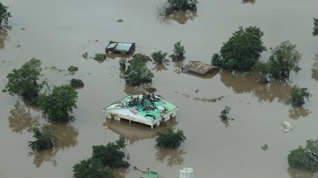 Mosambik: Eine Luftaufnahme zeigt überschwemmte Landschaft und Menschen, die auf einem Dach Zuflucht suchen / © Katastrophenhilfeagentur INGC (dpa)