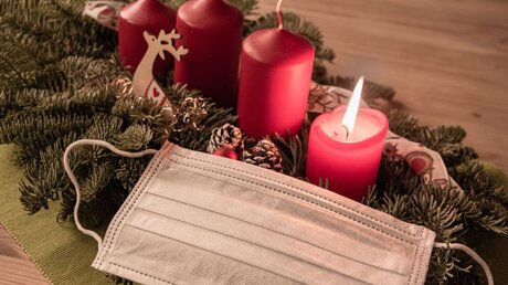 Mundschutz neben einem Adventsgesteck und Kerzen / © Nic-Art (shutterstock)
