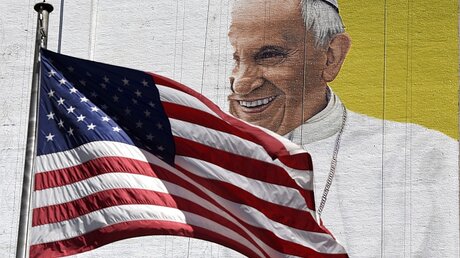 USA-Flagge vor abbröckelndem Papstbild / © Justin Lane (dpa)