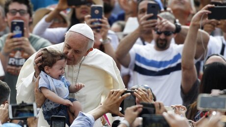 Papst Franziskus küsst bei der Generalaudienz ein kleines Kind. / © Riccardo De Luca (dpa)