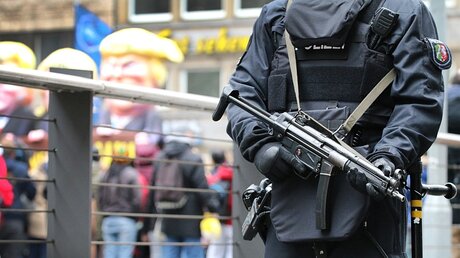 Ein mit einer Maschinenpistole bewaffneter Polizist steht am Rande des Rosenmontagszuges in Düsseldorf.  / © Henning Schoon (dpa)