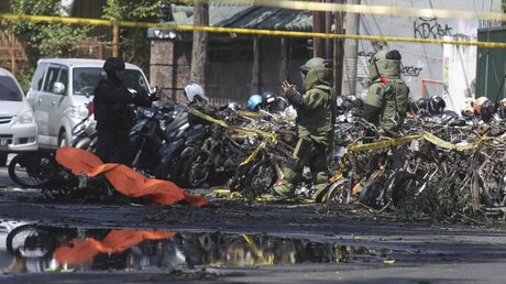 In Schutzanzügen untersuchen Polizei-Beamte nach einer Explosion nahe einer christlichen Kirche abgestellte Motorroller. / © Trisnadi/AP (dpa)