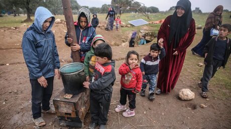 Syrische Frauen und Kinder stehen vor einer Höhle, in der mindestens acht Familien zusammenleben / © Anas Alkharboutli (dpa)