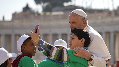 Vatikan: Ein Junge macht ein Selfie mit Papst Franziskus, als dieser zu seiner wöchentlichen Audienz auf dem Petersplatz ankommt. / © Andrew Medichini (dpa)