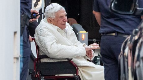 Der emeritierte Papst Benedikt XVI wird mit einem Rollstuhl in einen Bus geschoben / © Daniel Karmann (dpa)