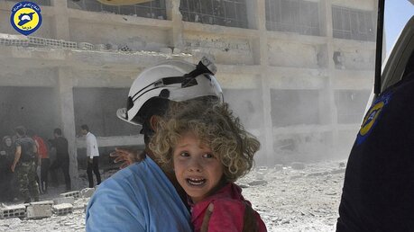  Das von der Syrian Civil Defense Gruppe, auch bekannt als Weißhelme herausgegebene Bild, zeigt einen Weißhelm, der ein Kind trägt  / © N.N. (dpa)