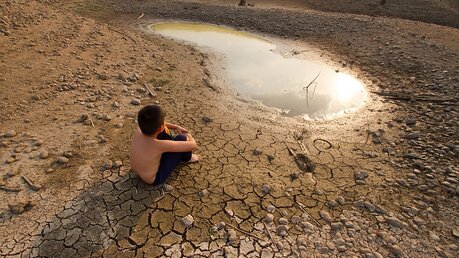 Ein Junge sitzt vor einer austrocknenden Wasserstelle / © Piyaset (shutterstock)