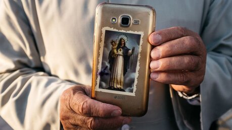 Ein Mann im Irak hält ein Handy mit einem Sticker, der Muttergottes mit Jesuskind zeigt in den Händen / © Jean-Matthieu Gautier (KNA)
