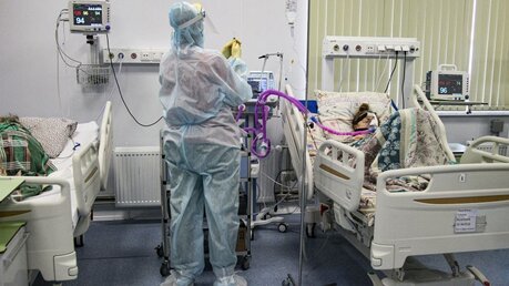 Ein medizinischer Mitarbeiter in Schutzkleidung behandelt einen Patienten auf der Intensivstation / © Roman Yarovitcyn/AP (dpa)