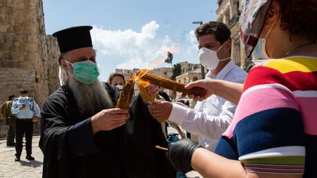 Ein orthodoxer Geistlicher mit Mundschutz gibt das "Heilige Feuer" an diplomatische Vertreter weiter / © Andrea Krogmann (KNA)