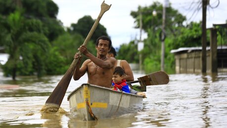 Eine Familie fährt mit einem Kanu durch eine überschwemmte Straße / © Stringer (dpa)