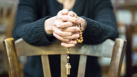 Eine Frau betet mit gefalteten Händen den Rosenkranz  / © Corinne Simon (KNA)