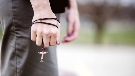 Eine Frau trägt eine Kette mit Kreuzanhänger / © Wirestock Images (shutterstock)