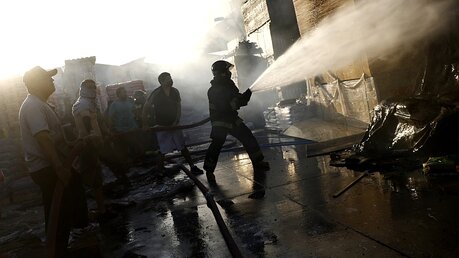 Feuerwehrleute löschen in einem von Demonstranten in Brand gesetzten Laden / © Mario Davila (dpa)