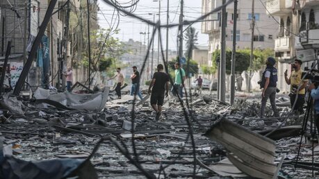 Gaza: Palästinenser inspizieren das Umfeld des schwer beschädigten Al-Jawhara-Turm / © Mohammed Talatene (dpa)