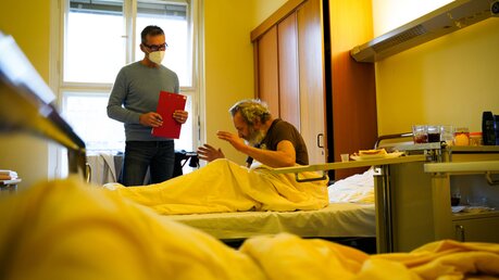 Der ehrenamtlich tätige Arzt Dr. Ingo Flessenkämper unterhält sich mit dem Patienten Manuel Müller in seinem Patientenzimmer am 8. Februar 2022 in Berlin / © Jannis Chavakis (KNA)