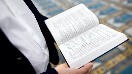 Ein Imam hält einen Koran in den Händen. / © Hauke-Christian Dittrich (dpa)