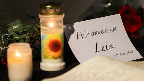 Ein Kondolenzbuch zum Gedenken an das getötete Mädchen liegt neben Blumen und Kerzen in einer Kirche aus. / © Oliver Berg (dpa)