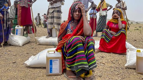 Menschen sitzen und stehen auf Säcken mit Lebensmitteln, die vom Welternährungsprogramm der Vereinten Nationen / © Claire Nevill (dpa)