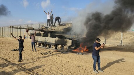 Palästinenser feiern an einem zerstörten israelischen Panzer am Zaun des Gazastreifens östlich von Khan Younis. Die islamistische Hamas hat vom Gazastreifen aus Israel massiv aus der Luft, am Boden und von See aus angegriffen / © Hassan Eslaiah/AP /dpa +++ dpa-Bildfunk +++ (dpa)