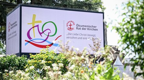 Logo der 11. Vollversammlung des Ökumenischen Rates der Kirchen (ÖRK) auf einer Tafel / © Anne Ackermann (KNA)