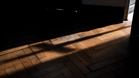 Der Schatten eines Kreuzes fällt durch die geöffnete Türe auf den dunklen Boden / © Harald Oppitz (KNA)