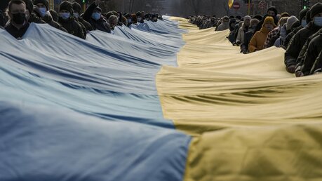 Menschen in Kiew tragen eine 200 Meter lange ukrainische Fahne durch das Olympiastadion. / © Vadim Ghirda/AP (dpa)