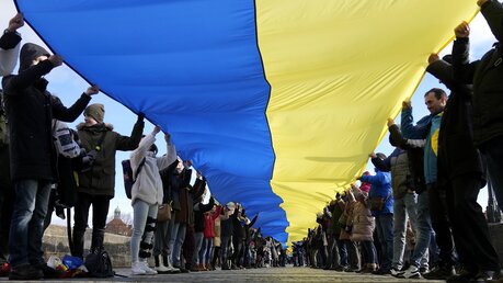 Protestteilnehmer in Tschechien halten eine große Fahne in den Farben der ukrainischen Nationalflagge hoch, um ihre Unterstützung mit der Ukraine deutlich zu machen. / © Petr David Josek/AP (dpa)