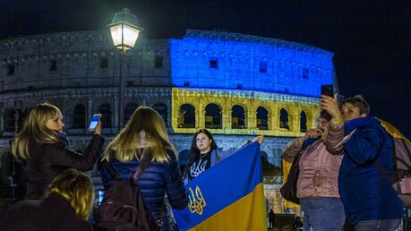 Rom: In Italien lebende ukrainische Staatsangehörige stehen vor dem Kolosseum, das in den Farben der ukrainischen Nationalflagge beleuchtet ist / © Domenico Stinellis (dpa)