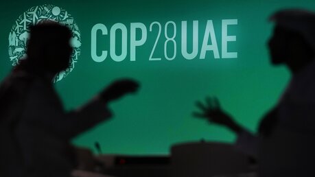 Unterhaltung vor einem Logo des UN-Klimagipfels COP28 / © Rafiq Maqbool/AP (dpa)