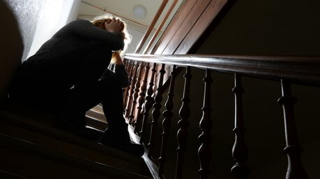 Symbolbild Angst: Eine Frau sitzt in einem Treppenhaus auf einer Stufe / ©  picture alliance (dpa)