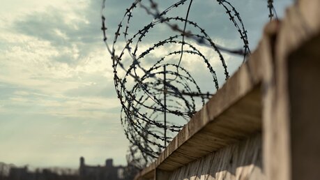 Symbolbild Stacheldraht über Gefängnismauern / © Vadzim Mashkou (shutterstock)